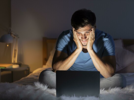 Late at night, a man stares at his computer screen, insomnia keeping him awake