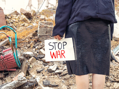 A young lady with a “stop war” sign against a backdrop of rubble, drawing attention to the human plight during wars