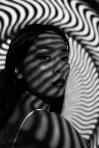 A contemplative woman sits near a black and white striped wall, her silhouette capturing the essence of philosophical thought and the quiet presence of inner awareness