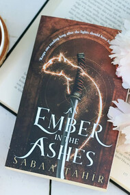 A cup of coffee and a copy of An Ember in the Ashes on a cozy wooden table