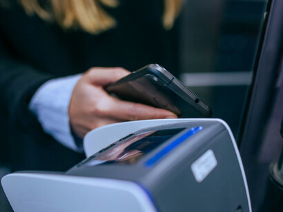 A woman holding a smartphone over a modern POS system demonstrates how far the world has come with digital transactions