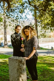 Mulher de camisa preta ao lado de uma lápide de concreto cinza enquanto segura uma flor