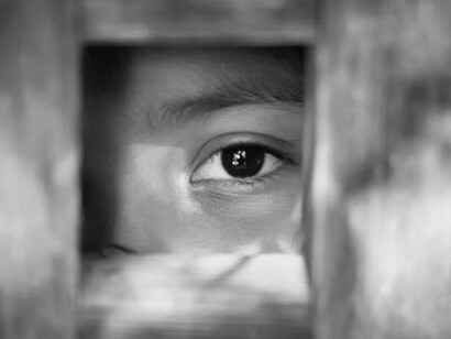 The empty gaze of a child standing behind what appears to be a wooden frame