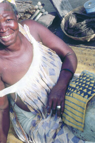 Ill. 1. Tonguoy Diarra pausing during the painting of the sleeve of a man’s tunic. The sleeve bearing the “Piece of a gourd” (Filen koloni) pattern is stretched across an empty calabash. Dyers always use the calabash as a support because it enables them to hold the metal spatula vertical to the cloth and to work on very small areas without staining other sections of the design. Kolokani.  
Photocredit Sarah C. Brett–Smith  
