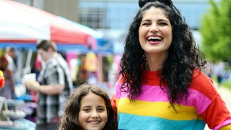 A woman in a rainbow sweatshirt with her child, symbolizing a queer family