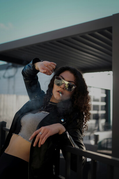 A stylish woman wearing sunglasses smokes outdoors