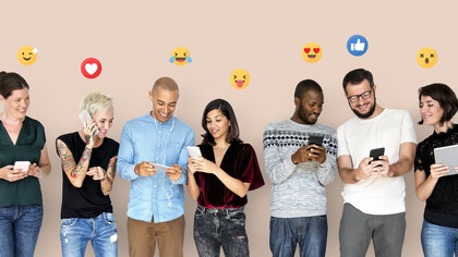Gruppo di persone che stanno utilizzando i loro dispositivi digitali, con varie emoji che fluttuano intorno a loro