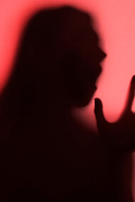 A silhouette of a woman stands gracefully behind flowing red curtains