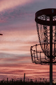 A silhouette of a man throwing a disc toward a disc golf basket