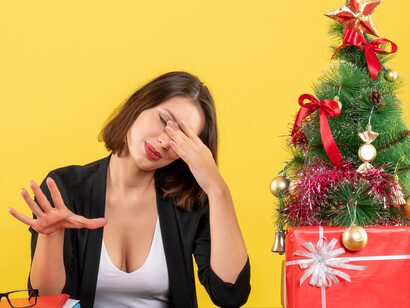 An exhausted, tense young woman seated at a table near Christmas decorations, reflecting the stress of preparing for the holiday