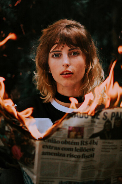 A girl playing with fire as she burns a newspaper, symbolizing the destruction of disinformation