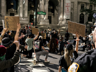 In New York, United States, a crowd of protesters kneels with raised arms, holding signs as part of an activist movement for justice and human rights