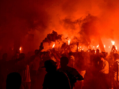 Anonymous individuals standing in the street, surrounded by smoke during protests at night