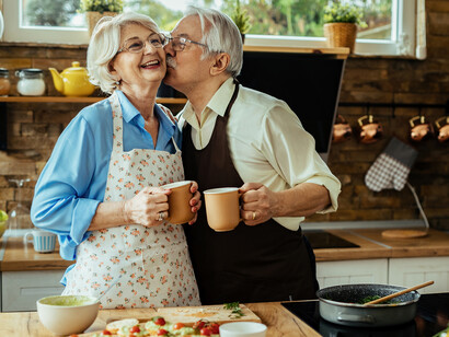 An elderly husband and wife laughing and dancing in their kitchen