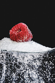 Colher cheia de açúcar e uma framboesa. O açúcar é uma fonte de energia para o corpo humano