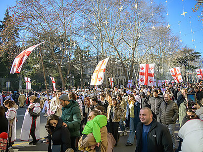 Demonstrators gather in an urban street in Georgia, raising Georgian flags as protest leaders address the crowd