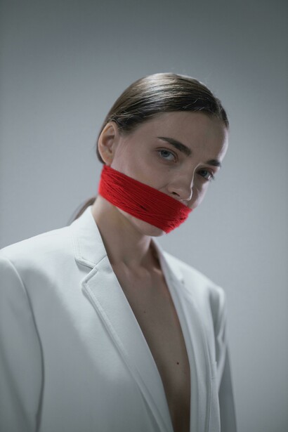 A woman in a white coat, her gagged mouth evoking silence as a metaphor, her presence an abstract reflection of stillness
