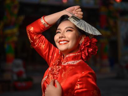A woman holding a few currency notes and decked in red for the Chinese New Year celebration, symbolizing the joy and prosperity that the traditional holiday brings to her culture.