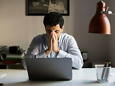 A tired man staring at his computer screen, feeling the weight of corporate burnout