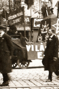 Cena de uma manifestação ou desfile ocorrido em 1º de maio de 1919 em Budapest, na rua Rákóczi, na antiga república soviética na Hungria. Na fotografia em preto e branco, pode-se observar signos políticos nas ruas