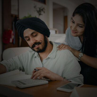 An Indian couple using a calculator and taking notes while budgeting their monthly living costs