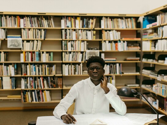 A male architecture student sitting at a table in the library, focused on his studies