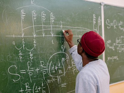 Rear view of a student working through a quantum mechanics equation on the chalkboard
