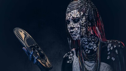A person from an indigenous African tribe wearing traditional makeup and costume while staring at a mask in their hand, symbolizing the struggle of the modern African youth caught between tradition and modernity