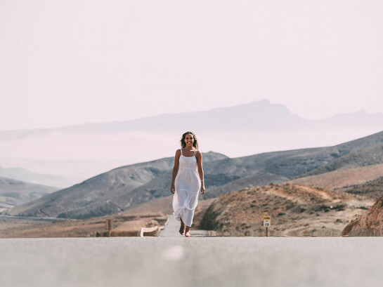 A woman walking on a road near hills under a cloudy sky, smiling, symbolizing her healing journey, spiritual warfare, and overcoming trauma, embodying peace and purpose