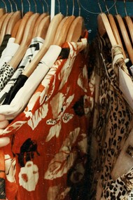 A woman rummages through a rack of colorful clothes at a thrift store