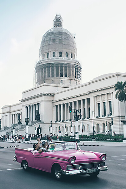 An old pink convertible coupe parked in front of the El Capitolio building in Havana, Cuba