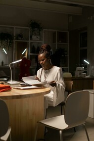A young African American fashion designer working late in her sewing workspace, a creative professional deep in thought