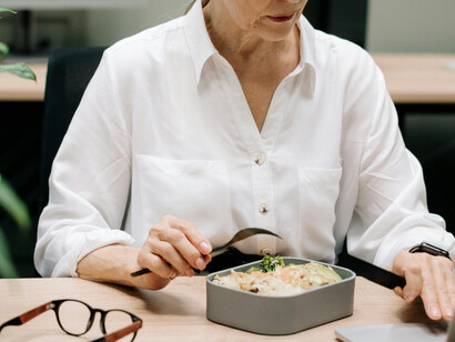 An elderly woman eating a balanced packed lunch at the office, reflecting healthy aging and mindful nutrition