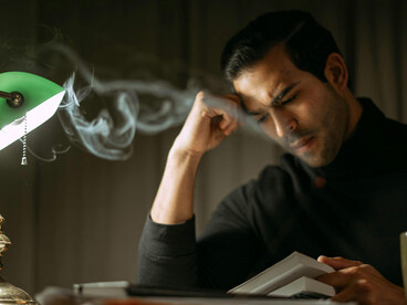A focused man reading by lamplight late at night, unable to slee