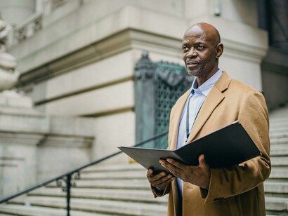 Focused black entrepreneur analyzing reports on city steps, representing ambition and vision