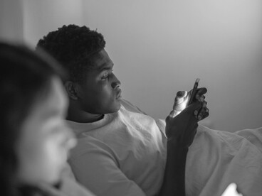 A couple lying in bed, each focused on their phones, highlighting disconnection and loneliness in the digital age