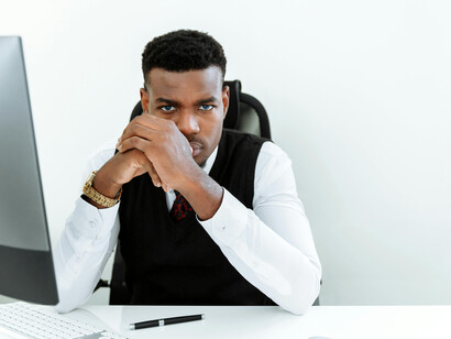 A Black man at his desk in the office, showing signs of stress and frustration