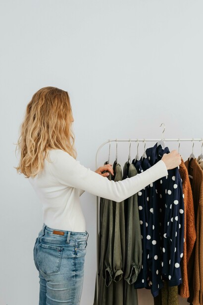 A woman dressed in a white long-sleeved top stands beside a neatly arranged clothes rack