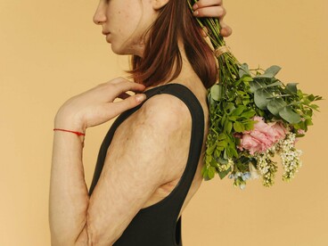A woman marked by burn scars holding fresh flowers, reflecting the grace found in perseverance