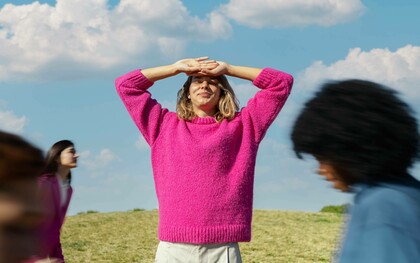 Donna all'aperto che si protegge gli occhi dal sole sorridendo: "Il giusto mix tra eyeliner e olio motore è la metafora di una donna che sa muoversi tra autonomia e connessione, indipendenza e interdipendenza, femminilità e prontezza"
