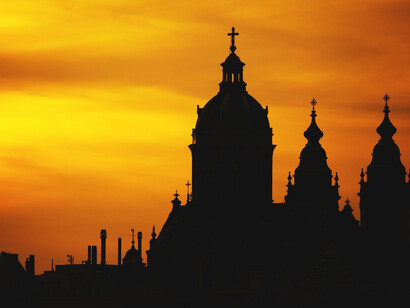 Church bell towers and domes in silhouette against a golden sky at sunset