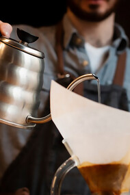Man pouring coffee from a pot into a filter, demonstrating the roasting process