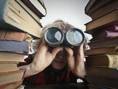 Homem com binóculos em meio à pilha de livros. É irônico: enquanto alguns apontam o dedo para ferramentas como o ChatGPT como as culpadas pelo empobrecimento intelectual, os números mostram que já estávamos produzindo adultos com severas limitações em leitura muito antes da era dos algoritmos. Cerca de 20% dos brasileiros ainda se encontram no nível rudimentar, mal conseguindo interpretar bilhetes simples. Isso é fruto de um histórico de desinvestimento secular na educação, não do recente avanço das tecnologias baseadas em IA. Culpar a tecnologia é, simplesmente, uma maneira conveniente de evitar enfrentar problemas estruturais há muito enraizados
