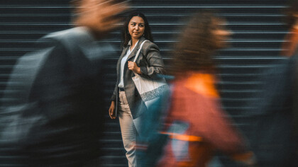 Pedestrians blur past a still woman standing on the street—embodying the tension between speed and stillness in an accelerated world