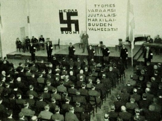 Reunião do partido nazista finlandês SKJ, 1933. Na parede, lê-se: "Libertem o trabalhador da mentira do judaico-marxismo"