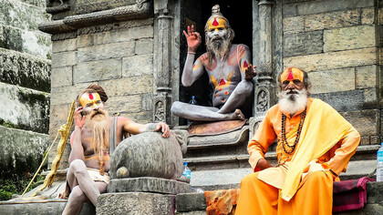 Three monks resting on the concrete steps of Pashupatinath Temple during the daytime, embodying the serene spirituality of Kathmandu, Nepal