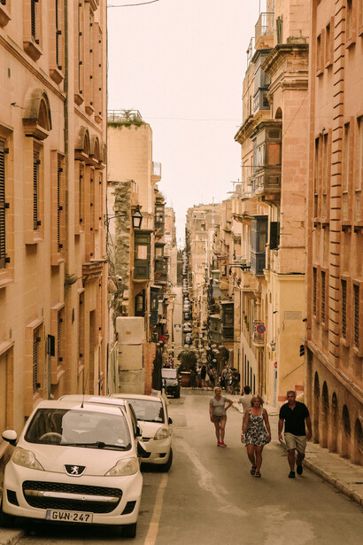 A group of people walking down a street next to tall buildings, Valletta, Malta 