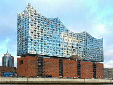 The Elbphilharmonie, commonly known as the Elphi, is a concert hall located in Hamburg’s HafenCity district on the Grasbrook peninsula of the Elbe River in northern Germany. Its striking design, resembling a billowing sail, ocean wave, iceberg, or quartz crystal, rises atop a historic brick warehouse adjacent to the city’s famous Speicherstadt