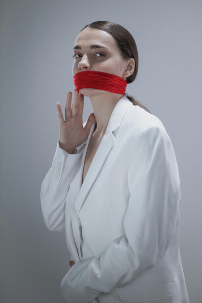 A woman in a white coat with a gagged mouth, symbolizing silence as a metaphor and stillness as an abstract expression