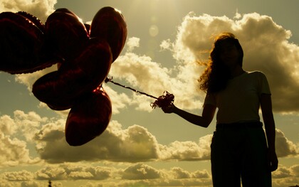 A woman holding a bunch of red heart-shaped balloons